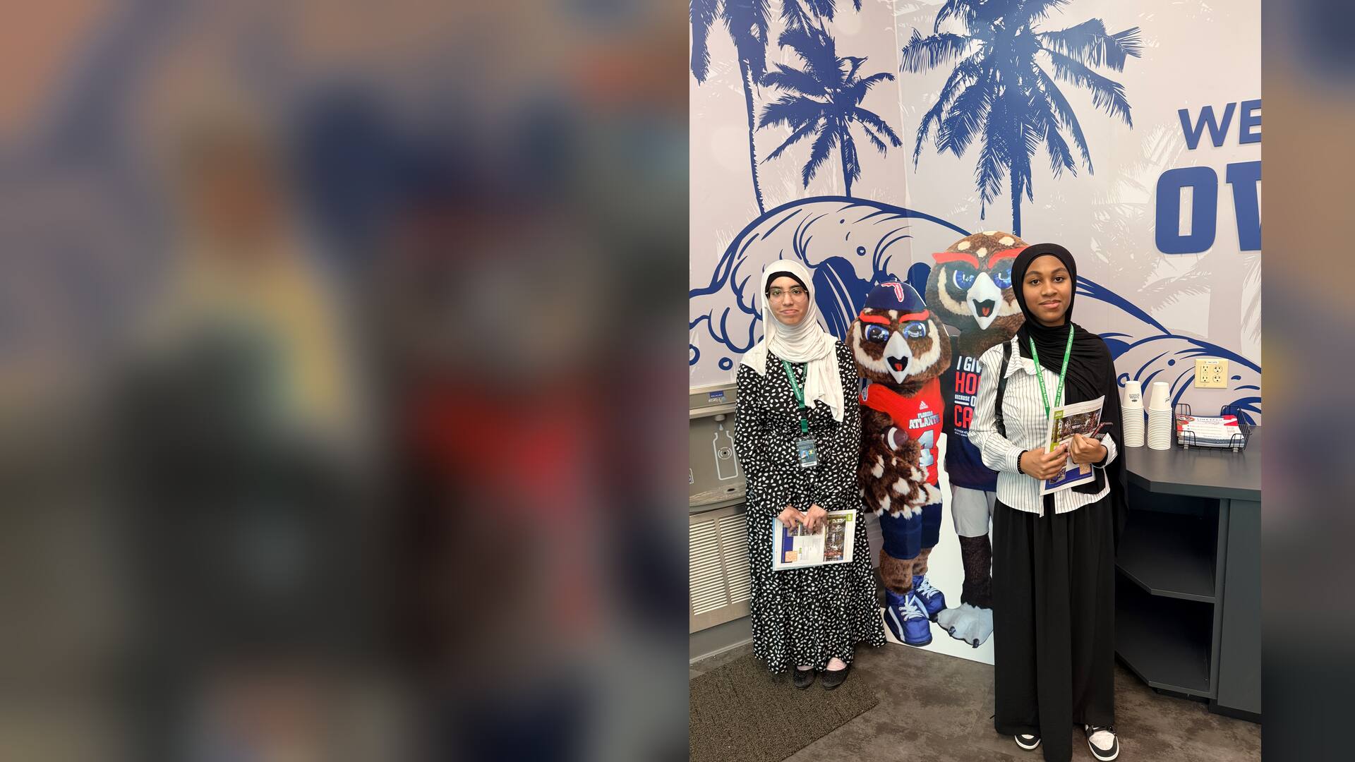 Two visitors with FAU brochures beside a cut-out of the owl mascot