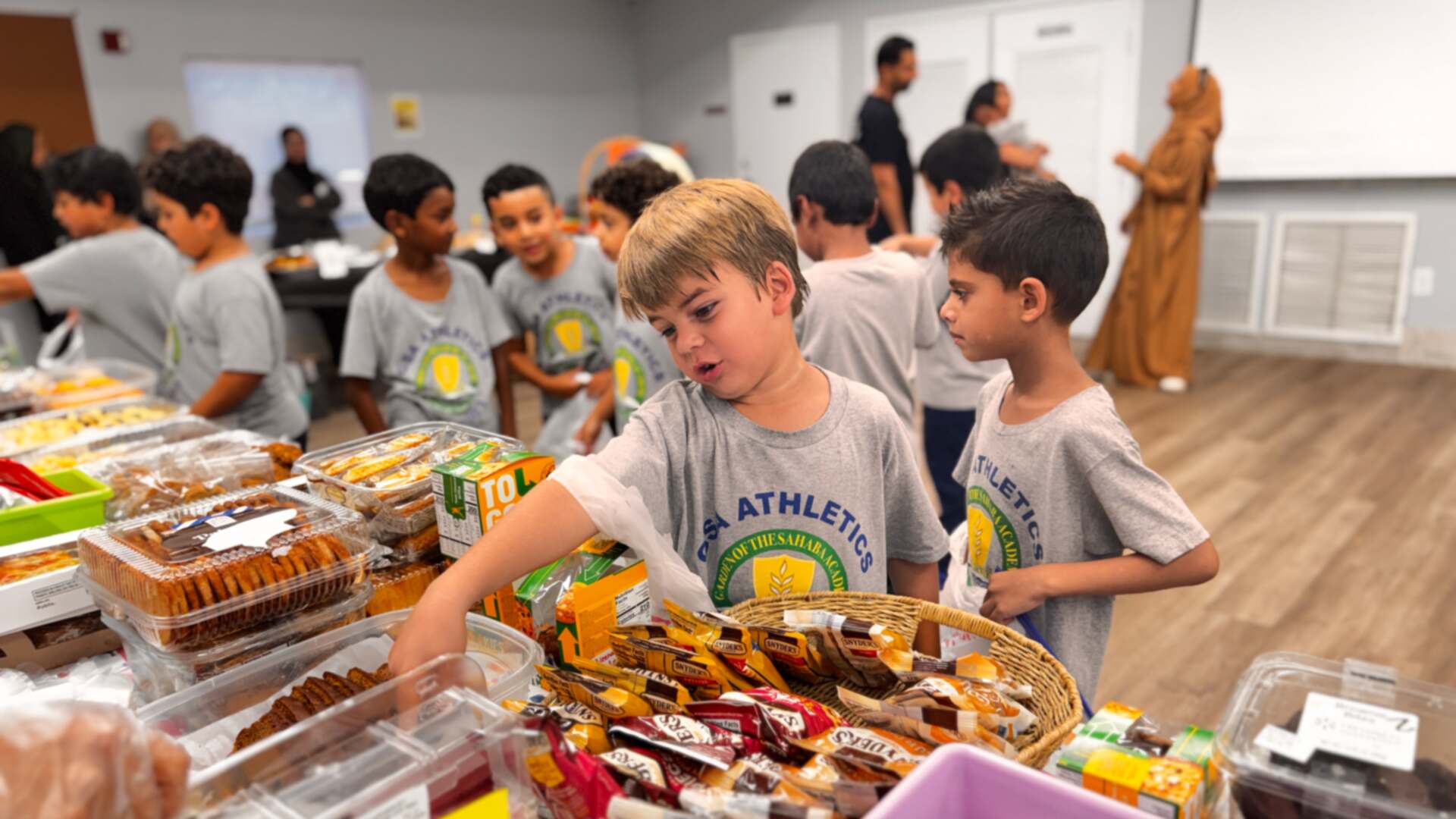 A young student reaches into a basket of snacks as classmates line up