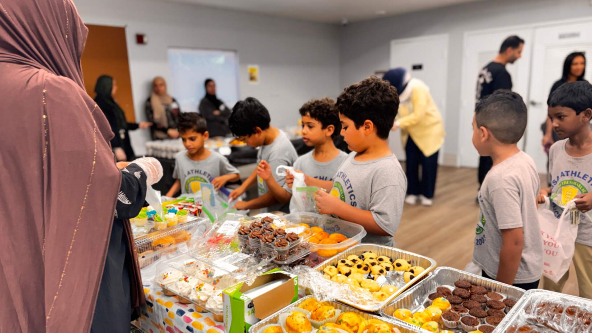 Classmates fill their bags beside trays of muffins and brownies