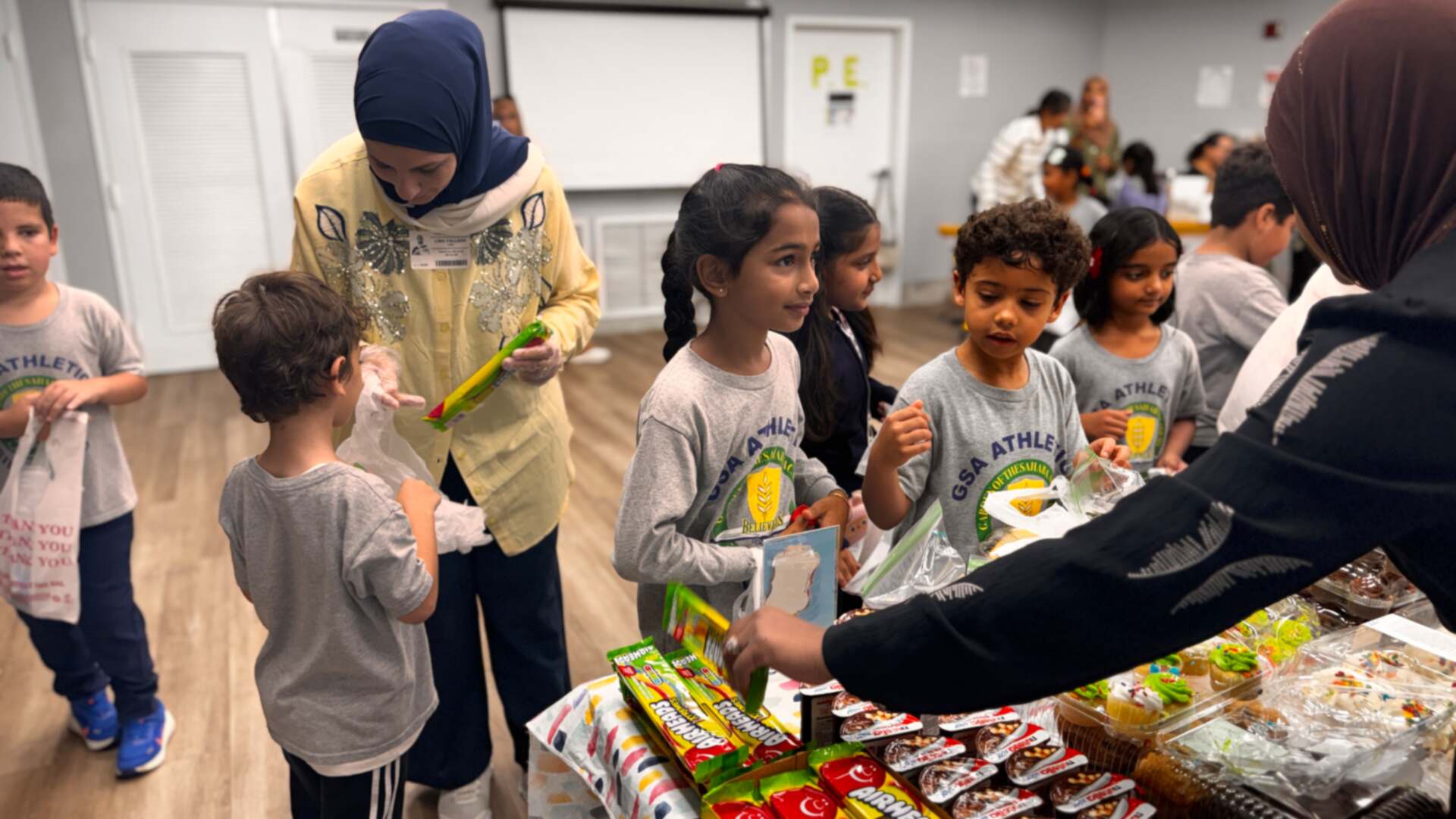 Young students choose packaged treats while volunteers help out