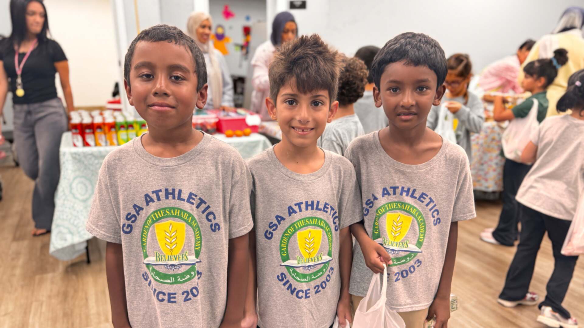 Three students in GSA Athletics shirts stand side by side with their bake sale bags