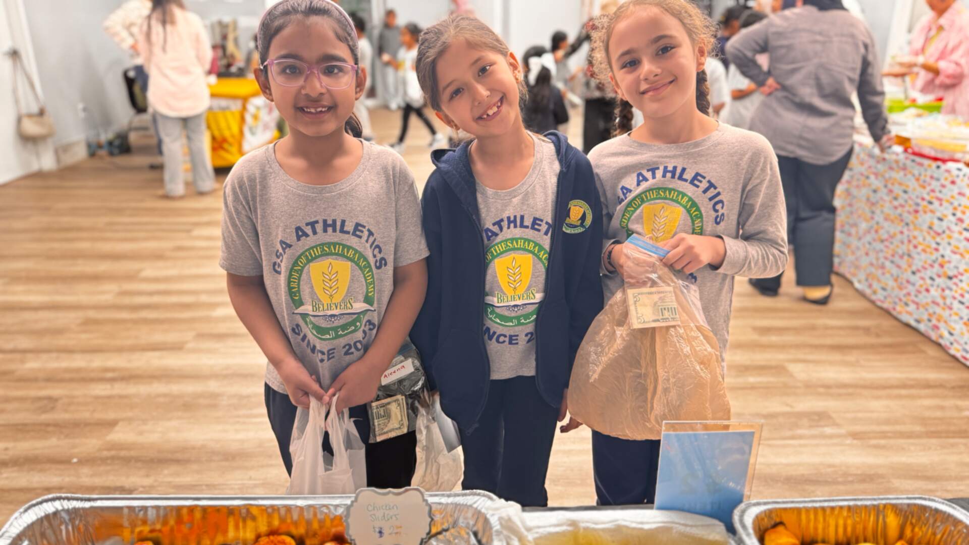 Three smiling students line up at a table of savory pastries