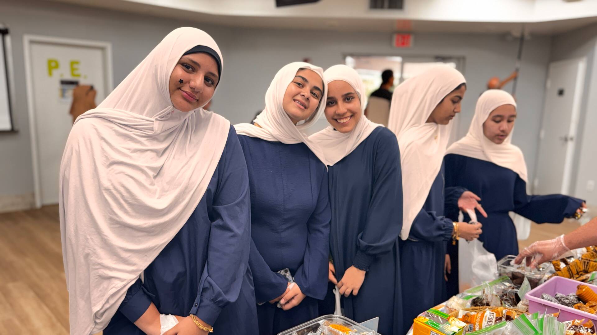 A row of older students smiles beside a table of snacks and baked goods