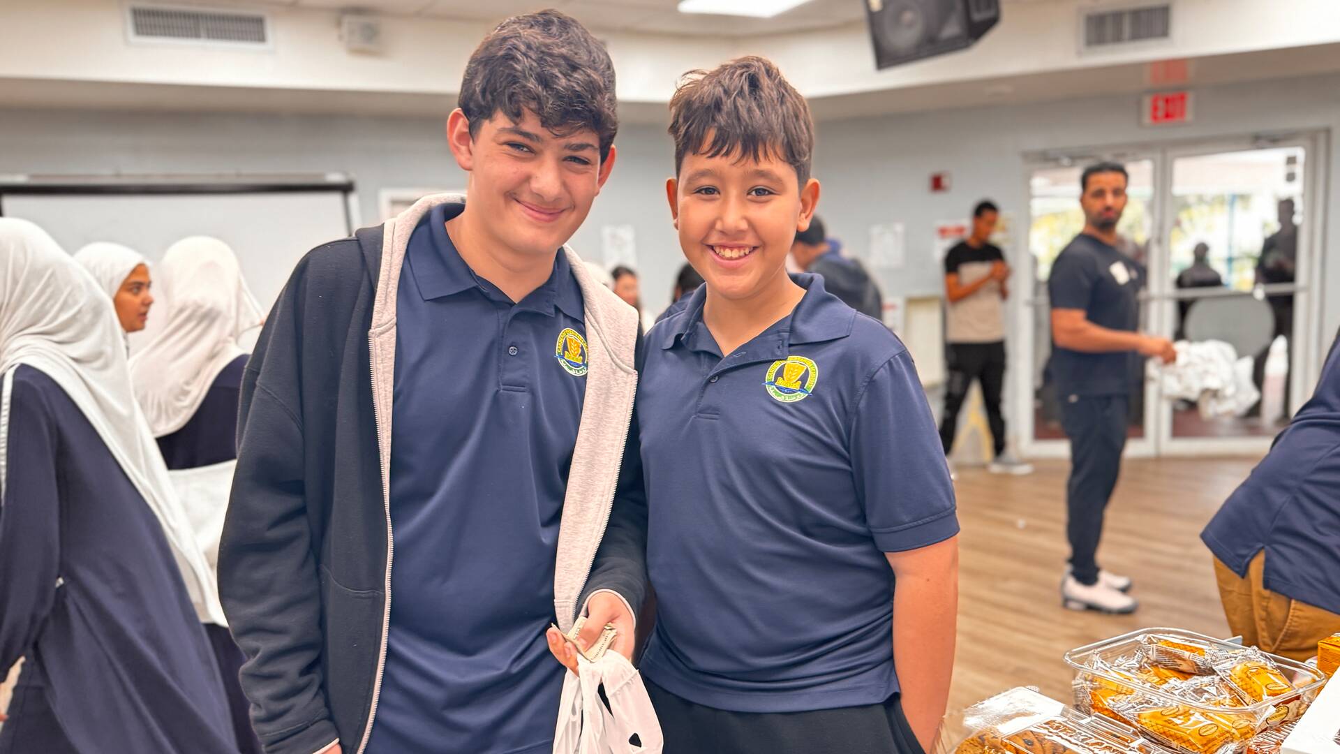 Two smiling students stand by a table of cookies with their bake sale bag