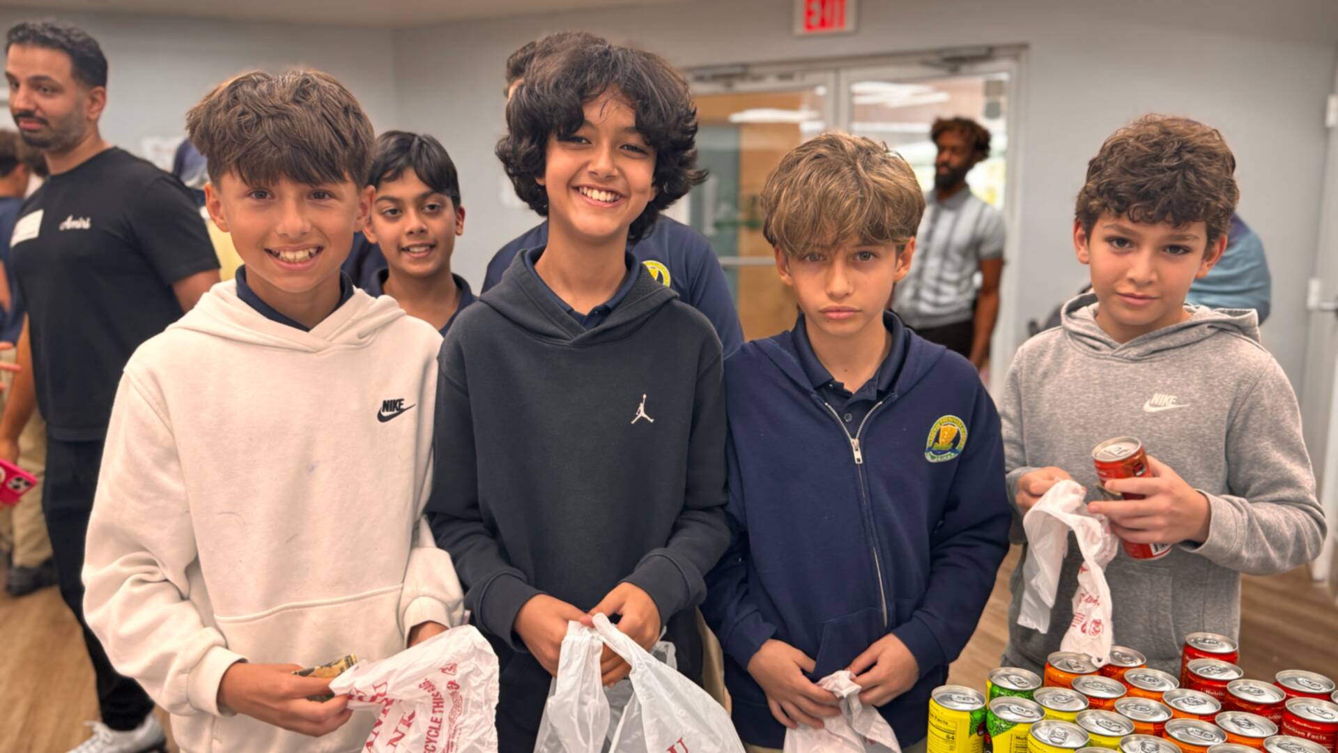 A group of students grins at the drinks table, bags of goodies in hand