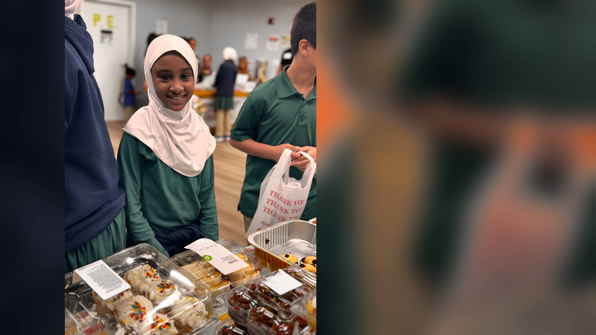 A student smiles brightly over a table of cupcakes