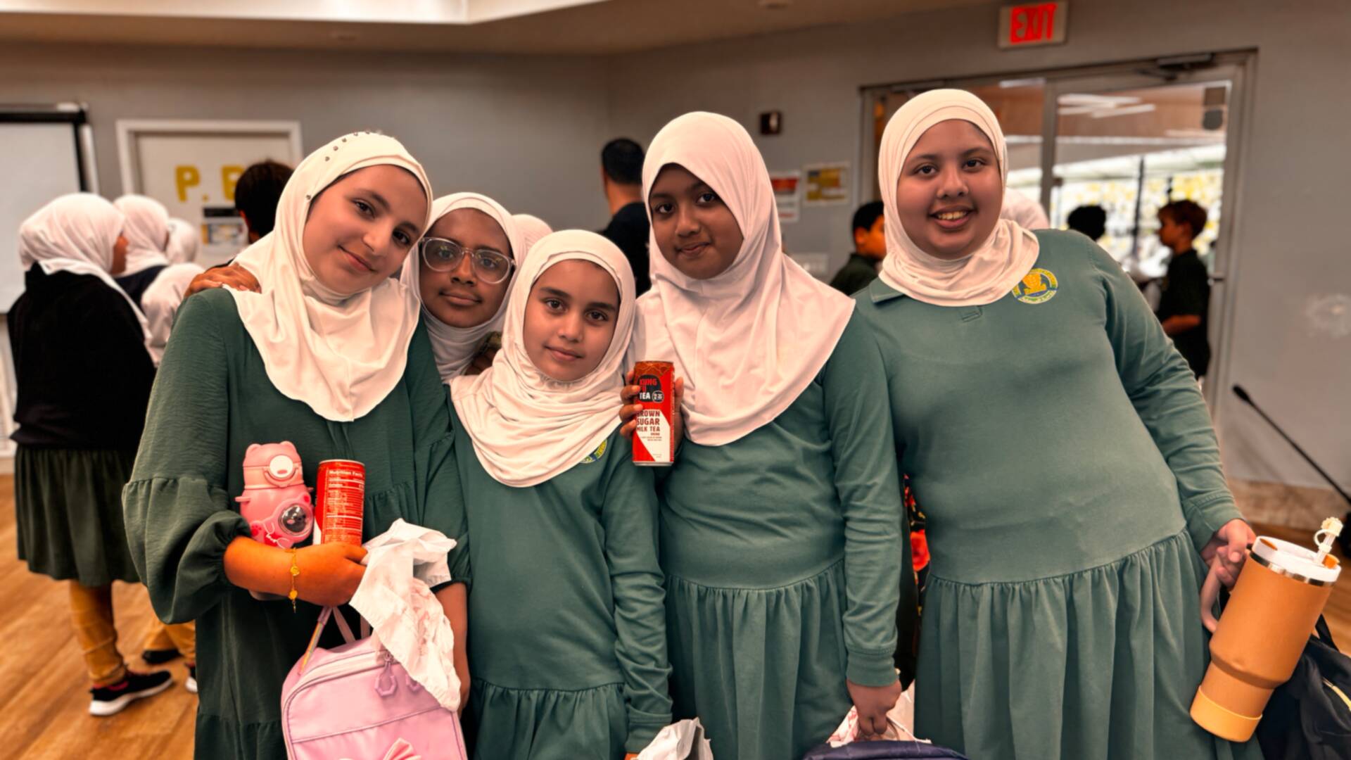 A cheerful group of students gathers close with their drinks and lunch bags