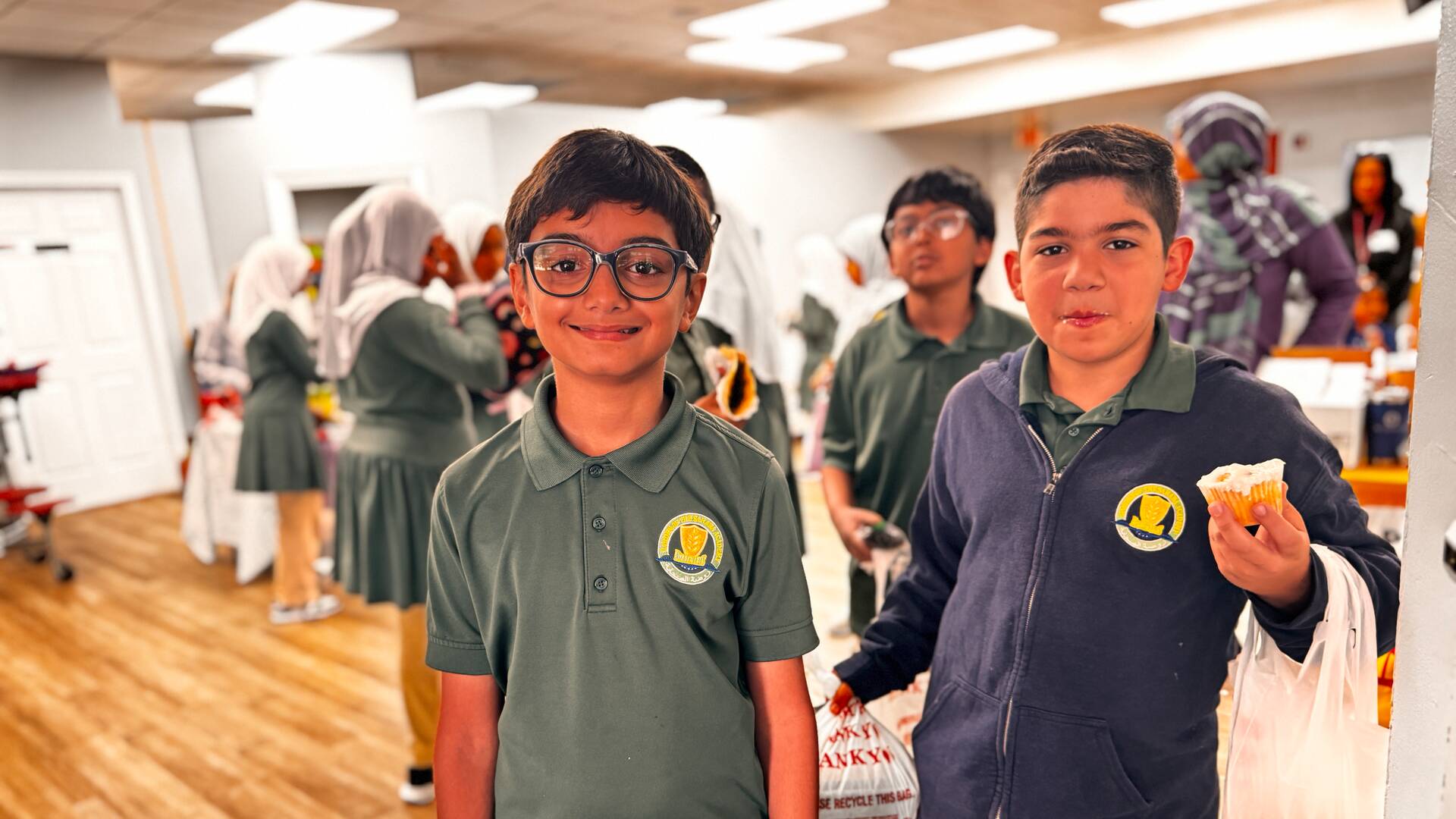 Two smiling students show off their bags and a cupcake