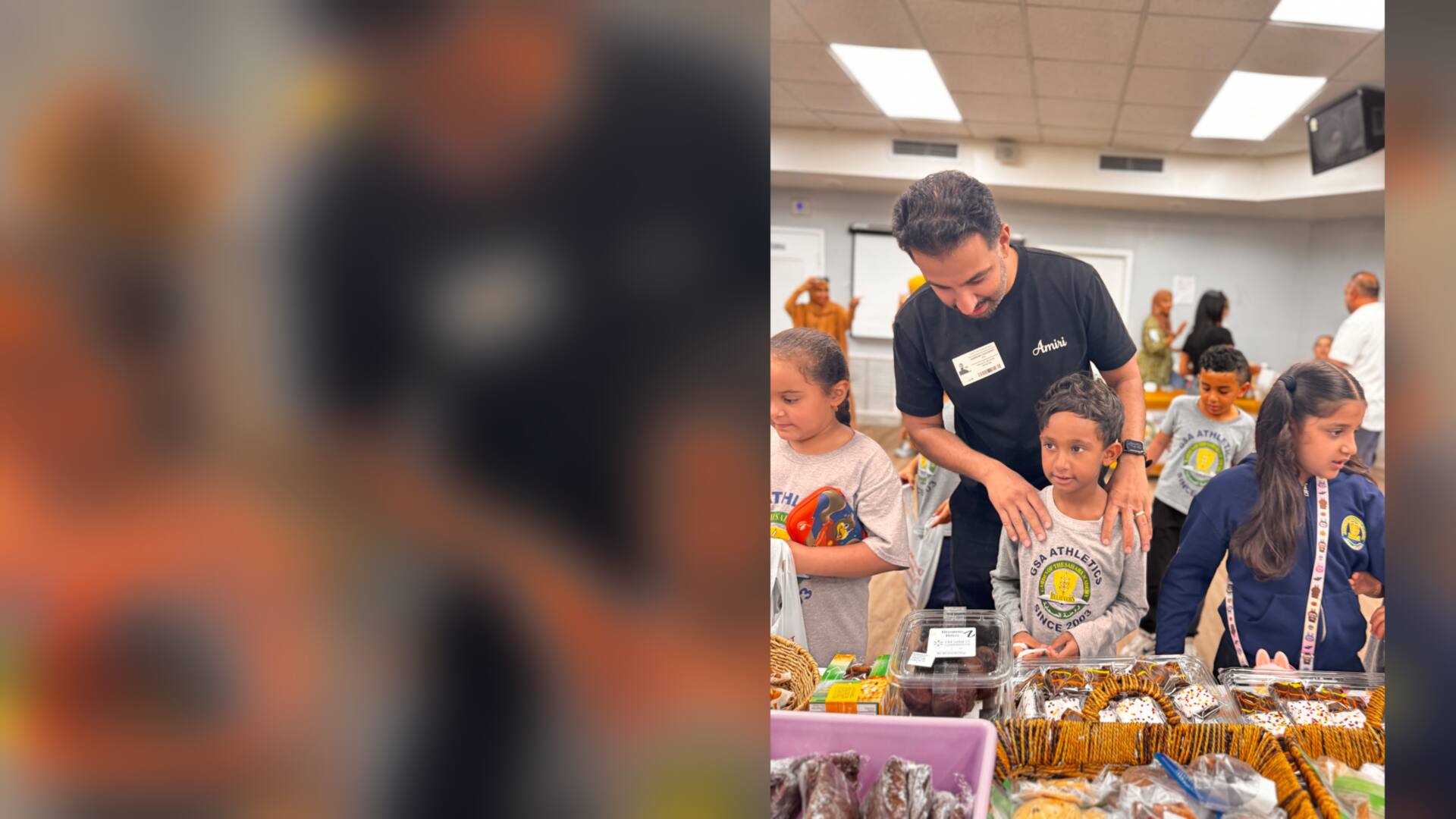 A volunteer rests a hand on a young student's shoulders at the treat table