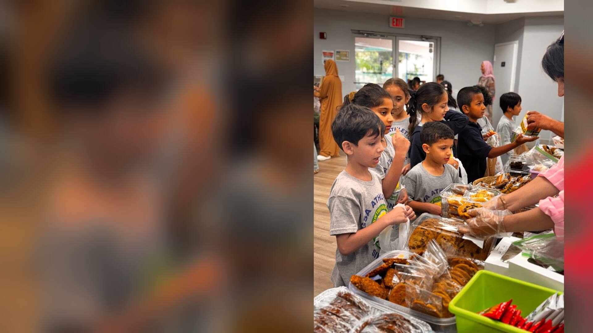 A line of young students waits as gloved hands pass out cookies