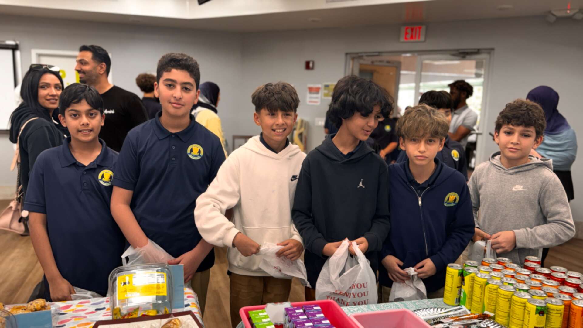 A row of older students stands behind the drinks and snack table