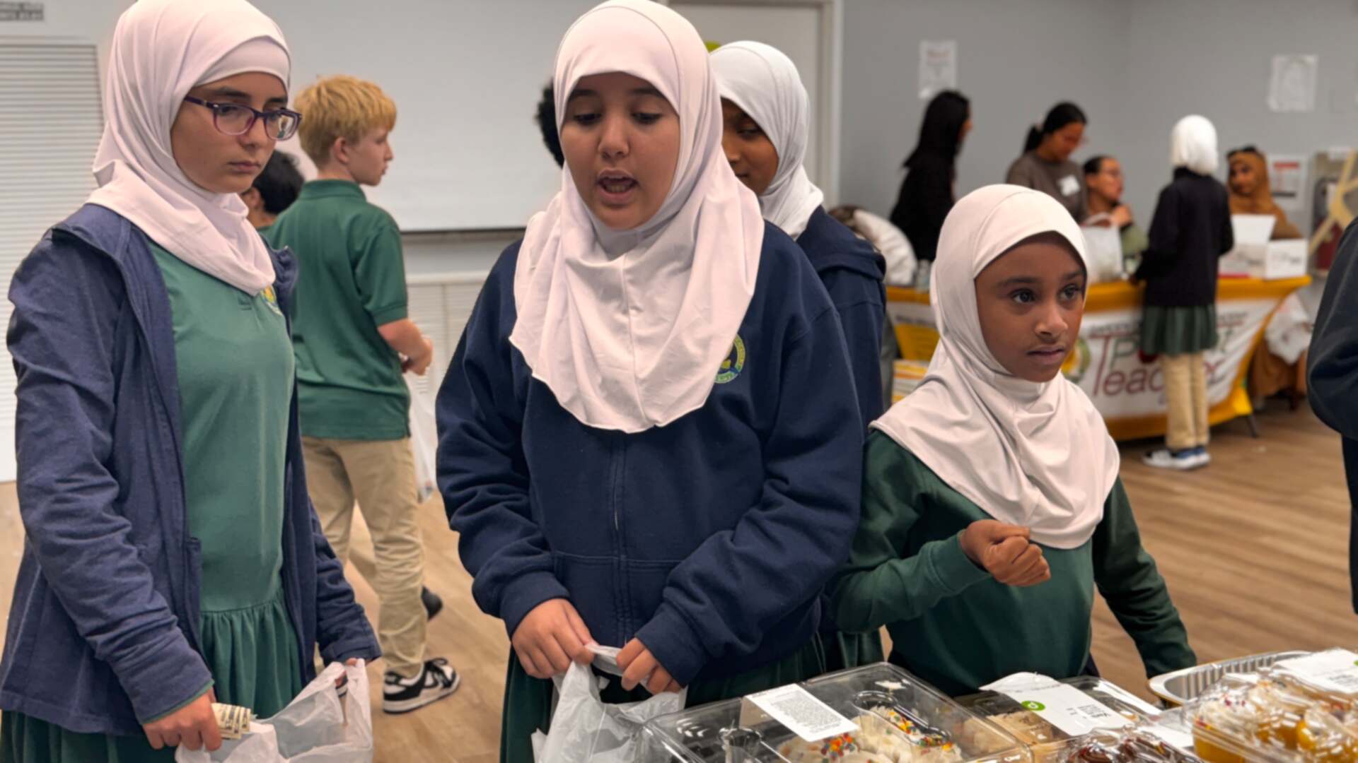 Students in green uniforms browse the cupcake table together