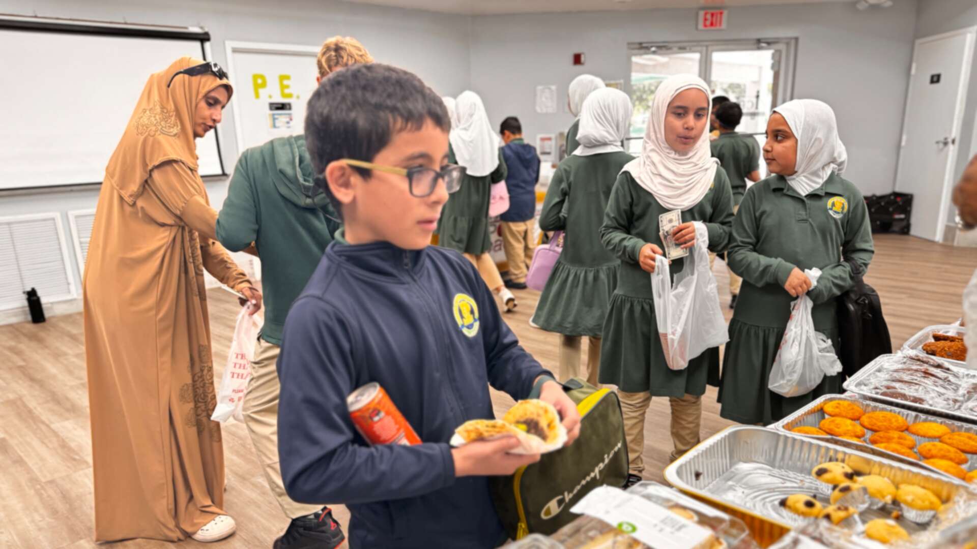 A student in glasses chooses a treat while classmates mingle nearby
