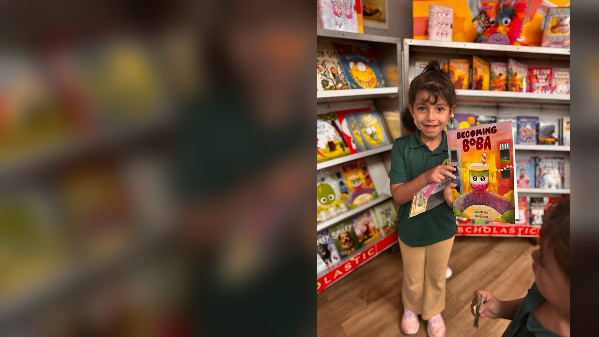 A smiling student showing a picture book in front of the shelves
