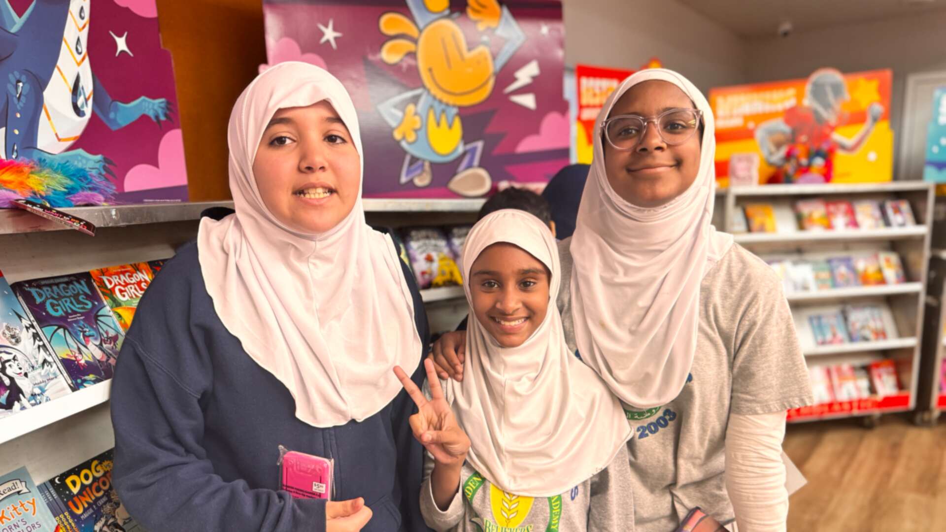 Three friends smiling together by the bookshelves