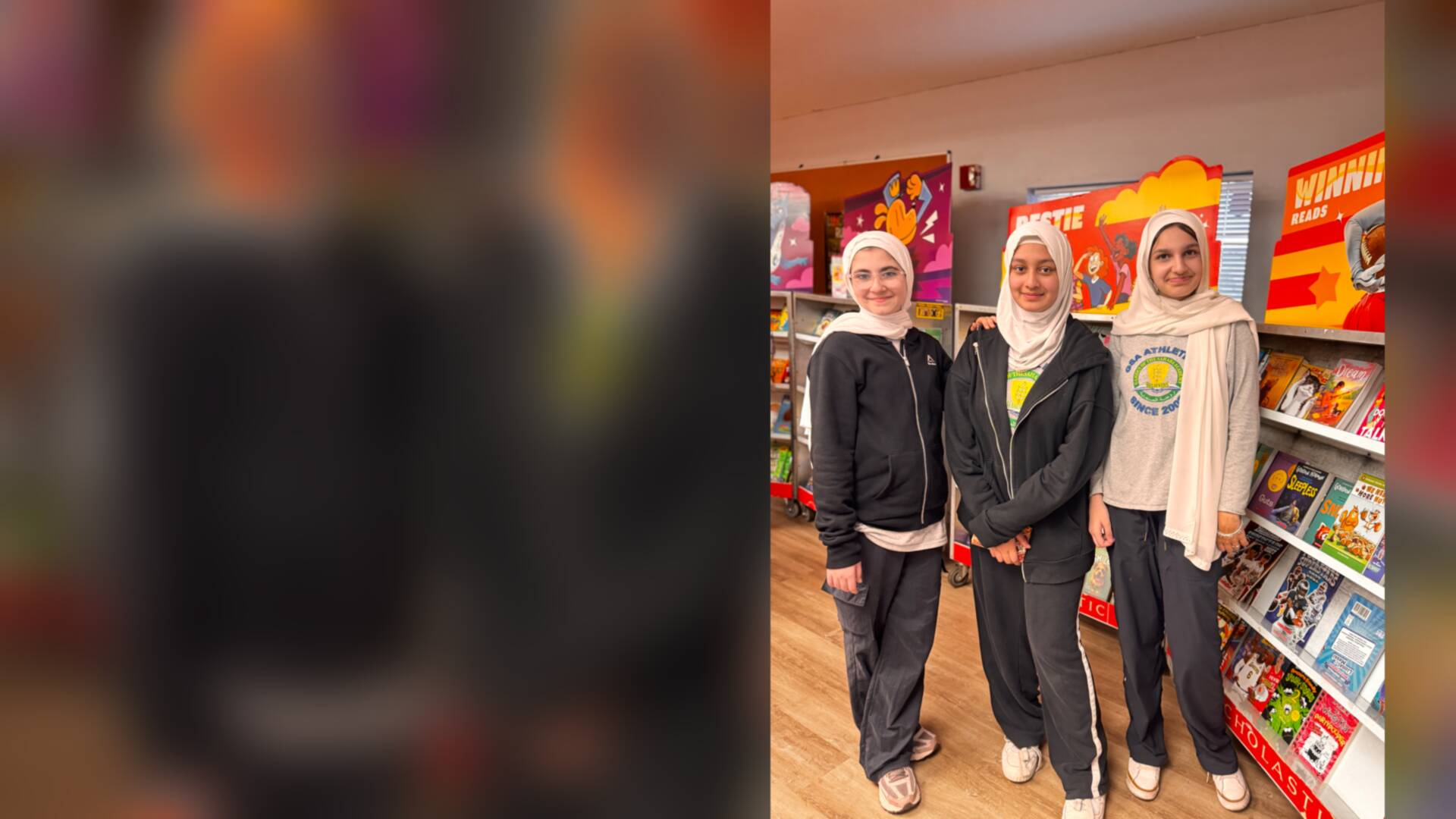 Three students posing beside the shelves of books