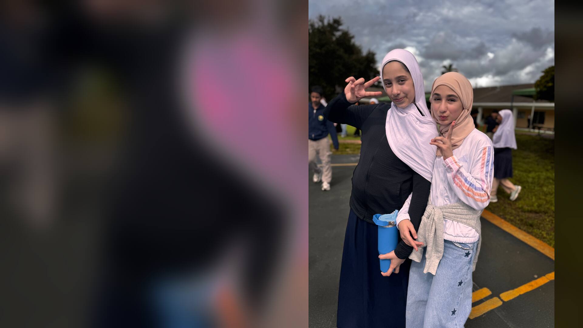 Two friends in soft pink and peach flash peace signs under cloudy skies