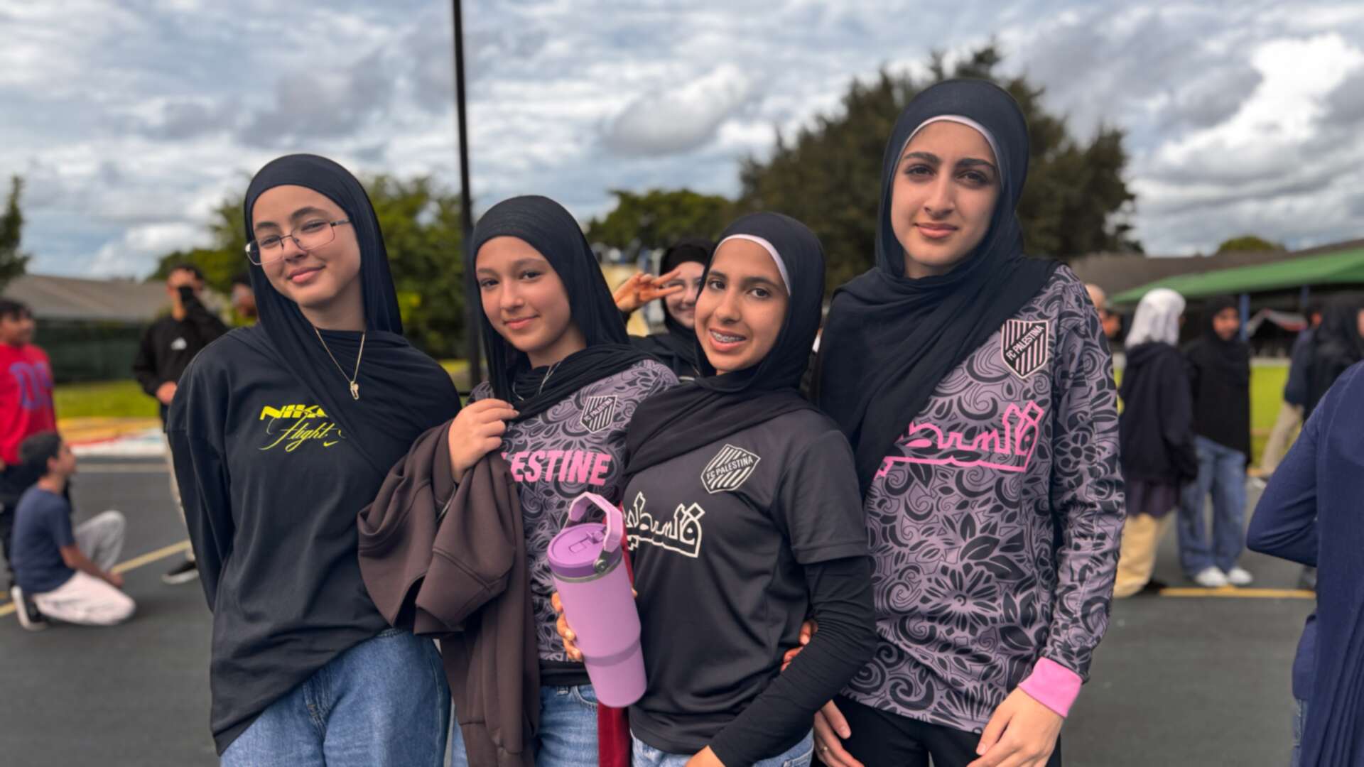 Four friends in black hijabs and patterned tops smile together outside