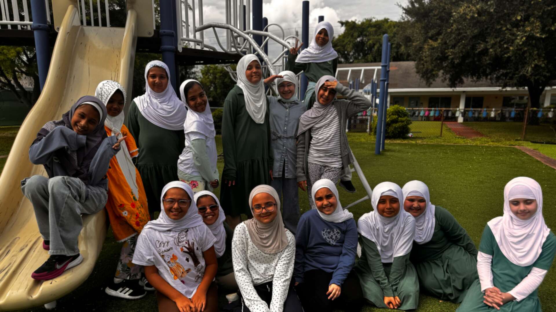 Smiling students in fall greens, golds and creams gather at the playground on Dress Down Day