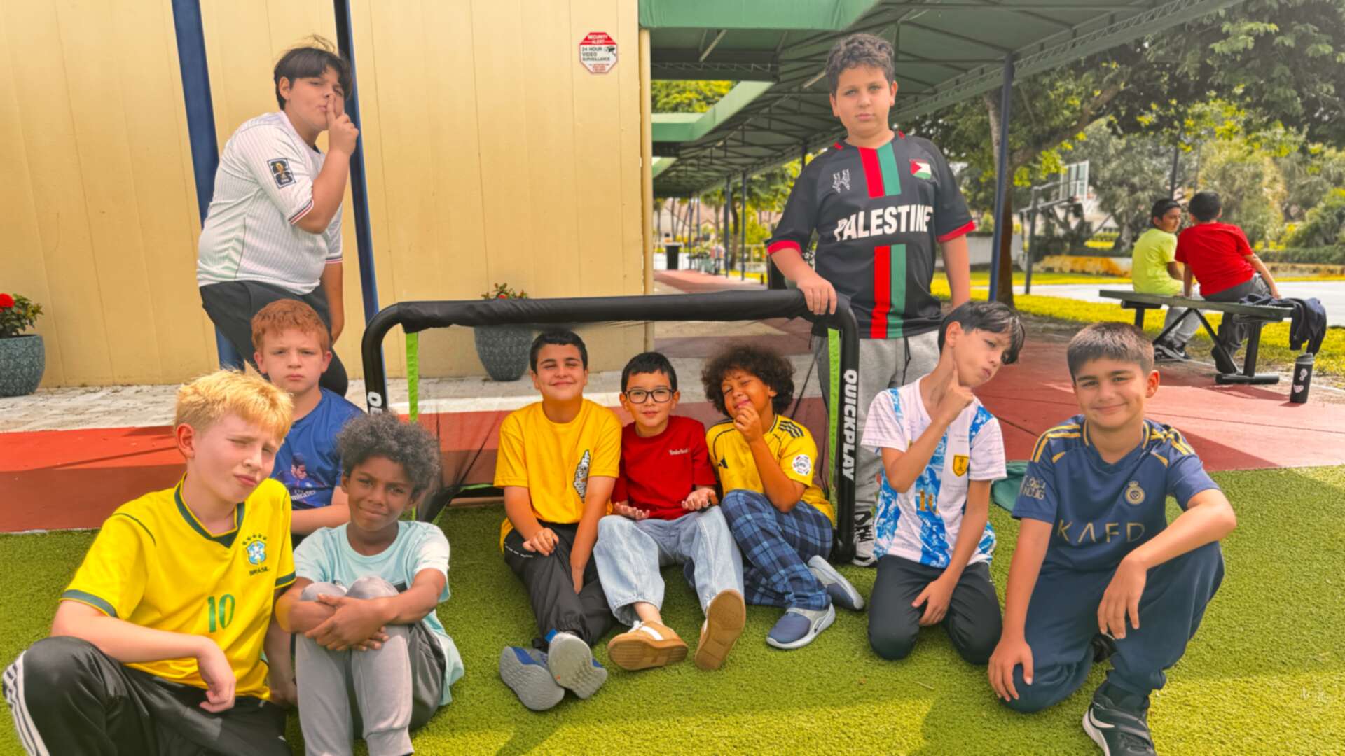 A crew of classmates in jerseys and bright tees gather around a mini soccer goal