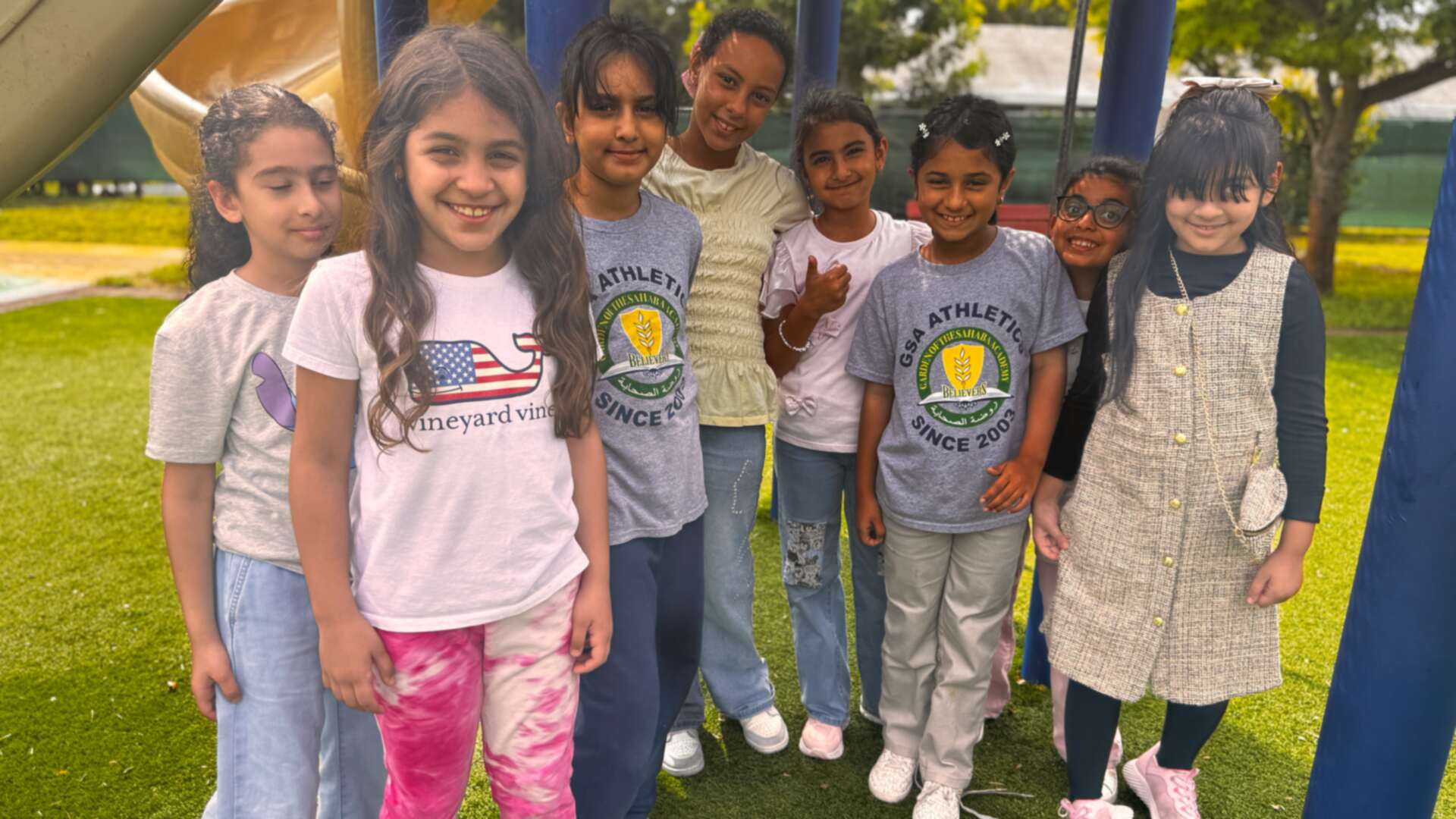 A cluster of smiling friends gathers under the playground on Dress Down Day