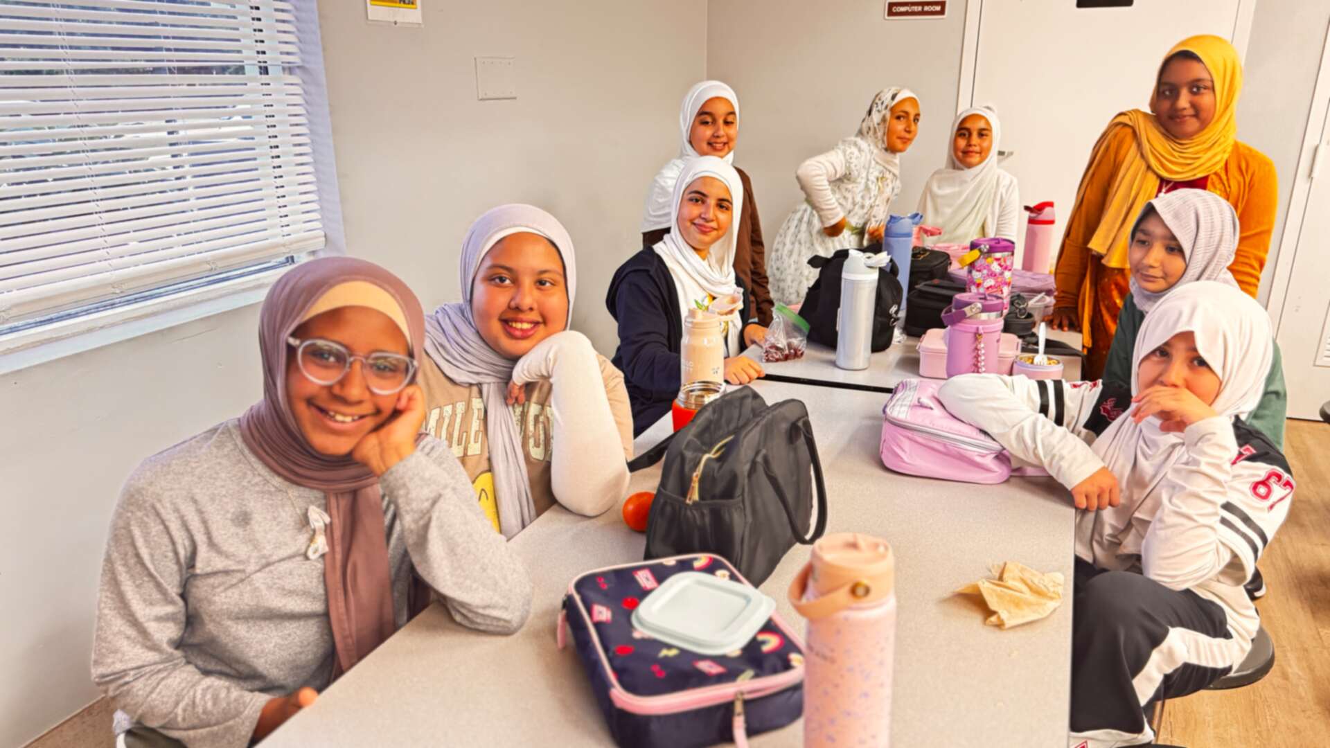 Classmates in mustard, mauve and cream smile around the lunch table