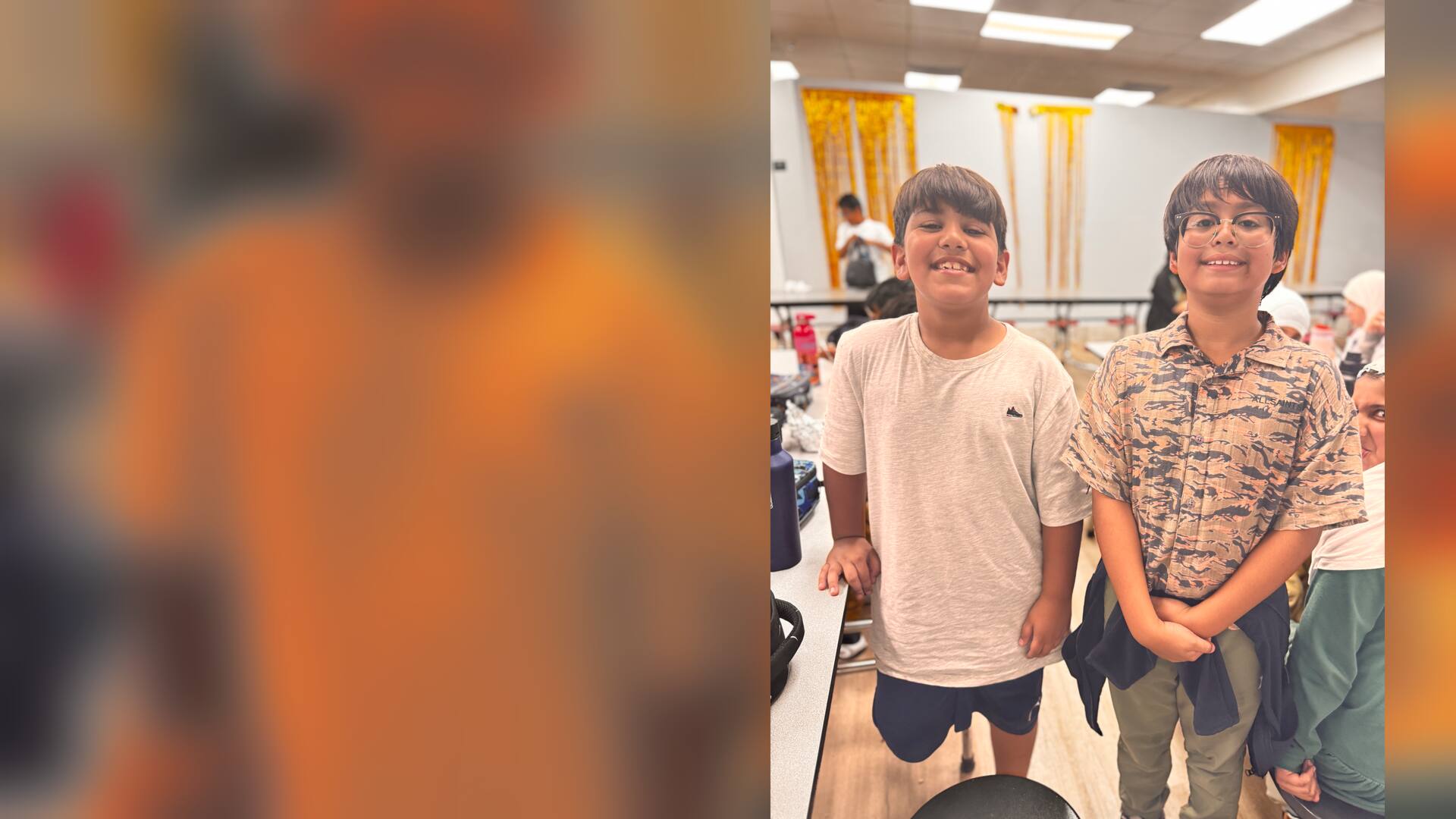 Two friends in a cream tee and patterned shirt grin in the lunchroom