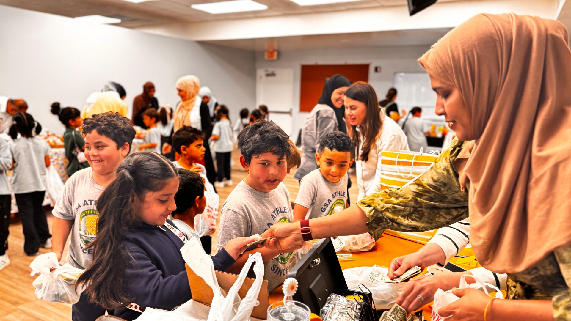 Young students hand over money to a volunteer at the bake sale cash box.