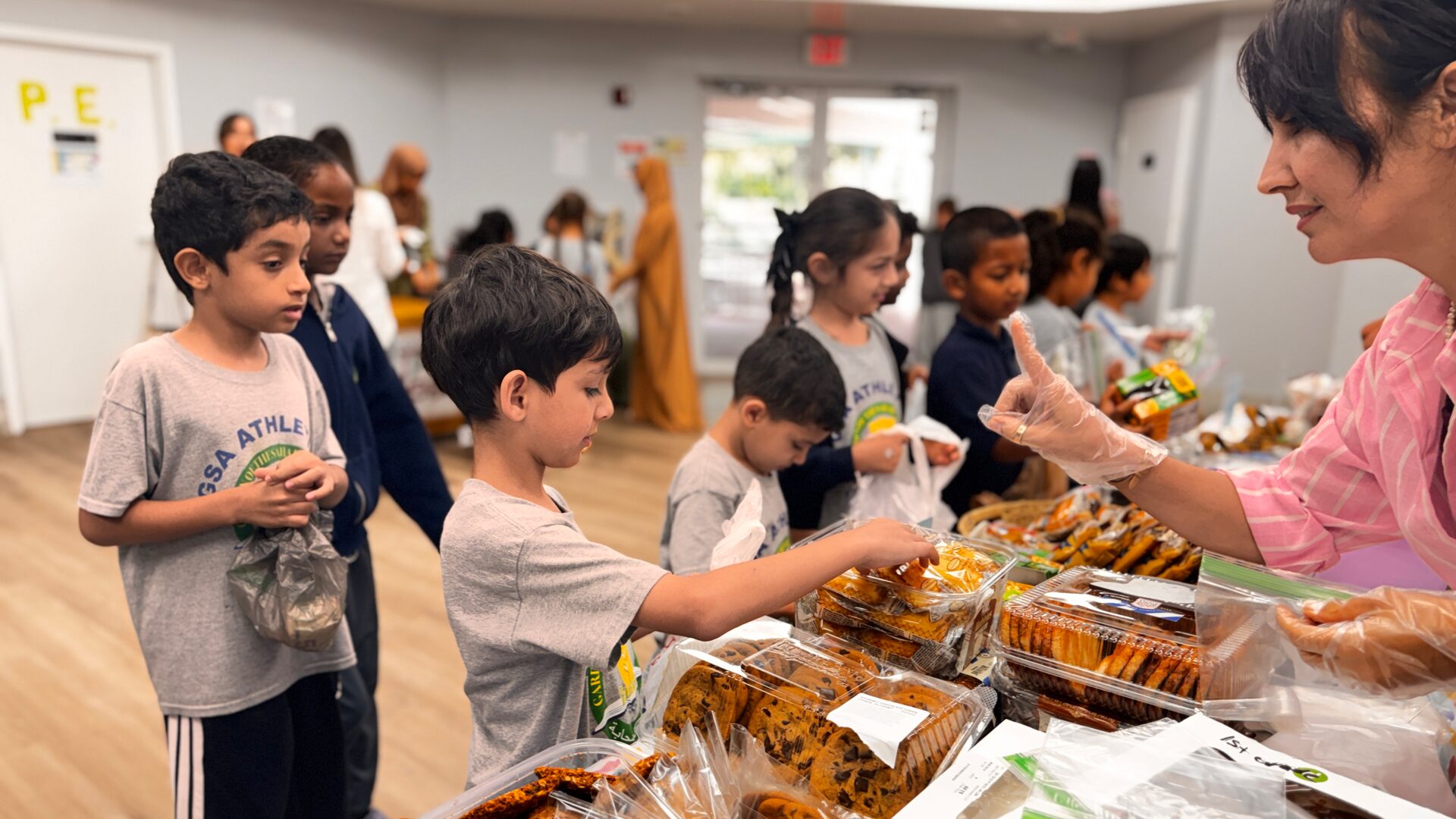 A young student reaches for a cookie as a volunteer serves from the bake sale table.
