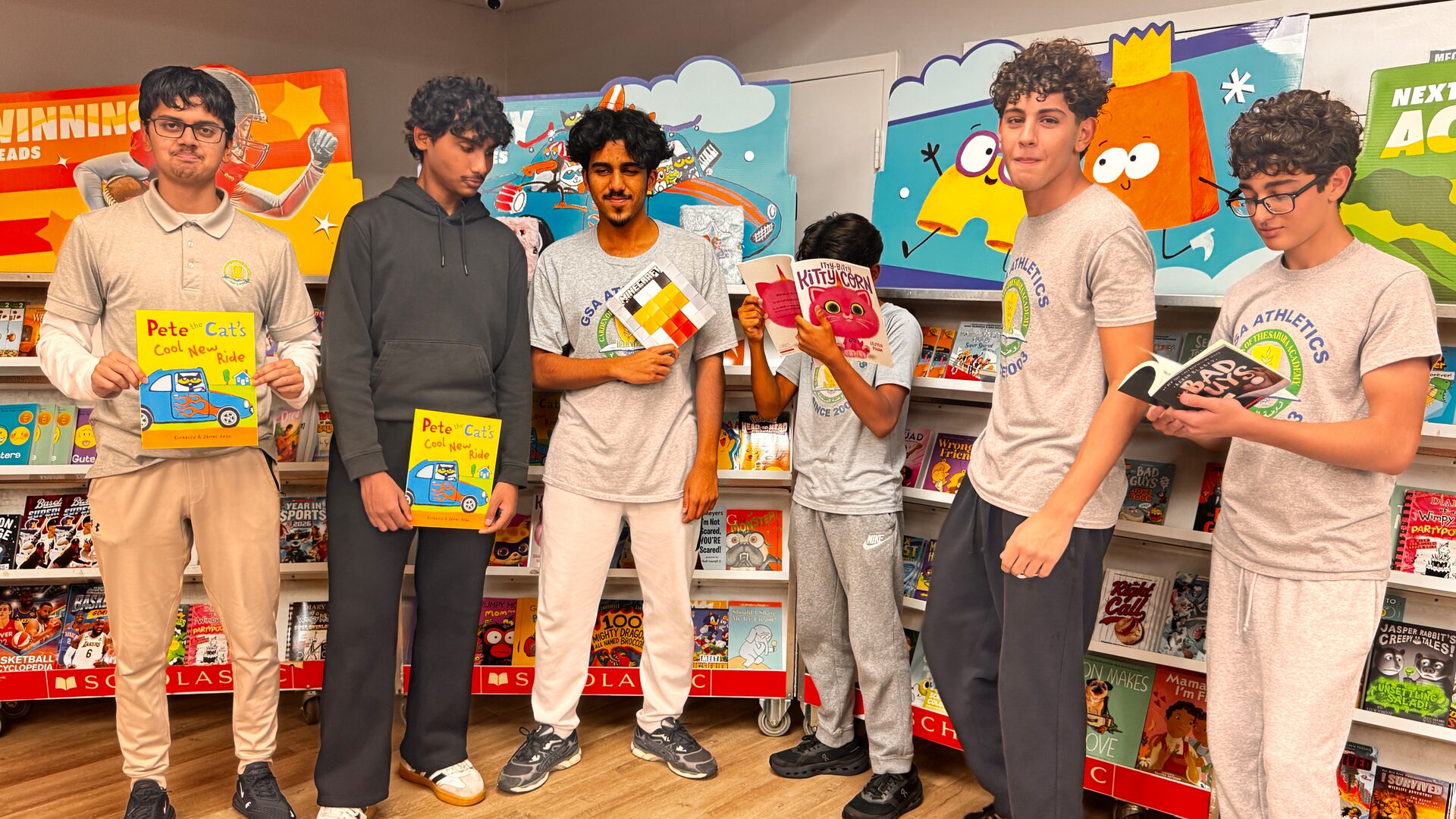 Six students stand in front of the book fair shelves, some holding up books.