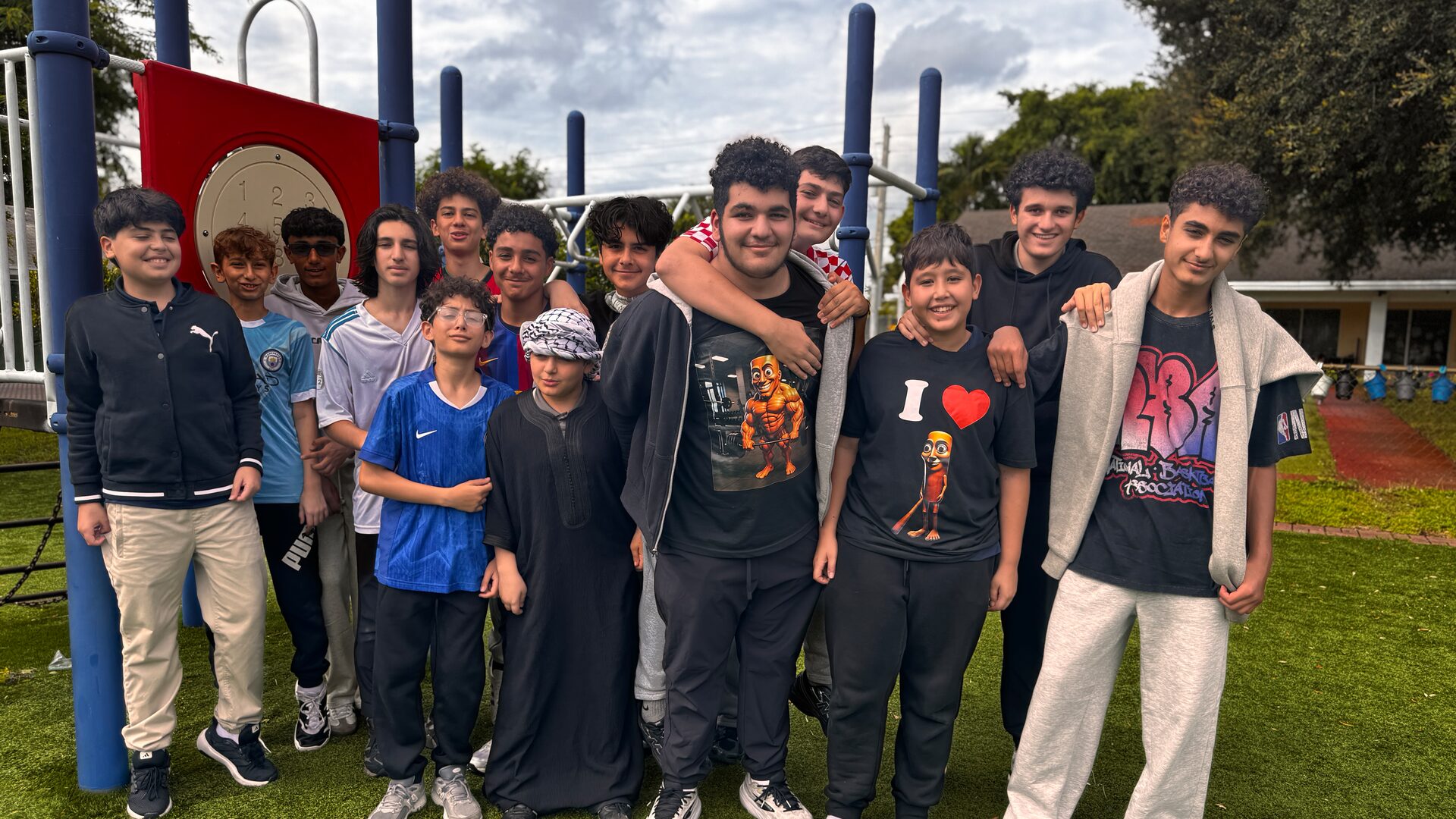 A large group of students in casual clothes poses together beside the playground.