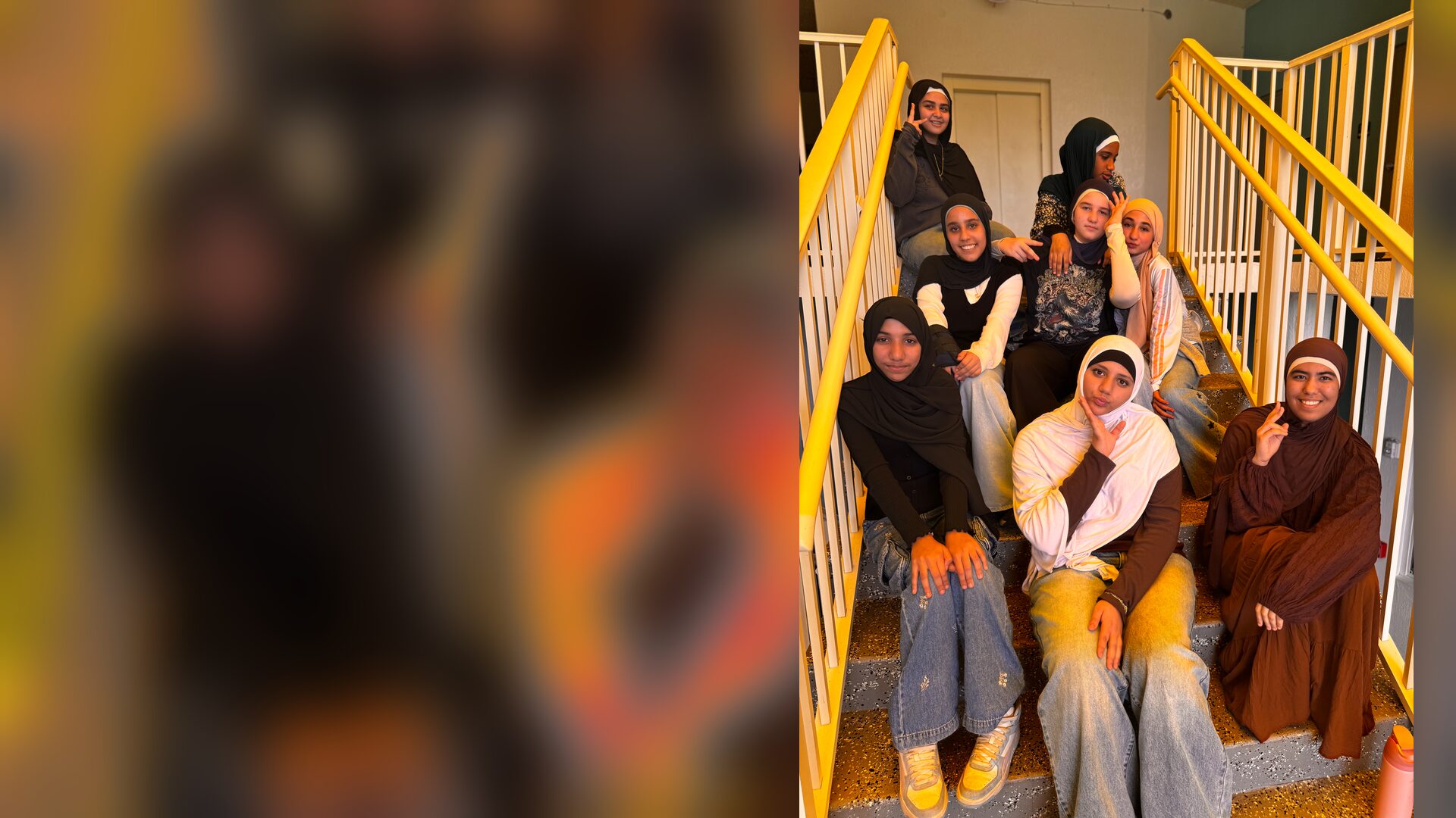 A group of students in everyday clothes poses together on a stairwell with yellow railings.