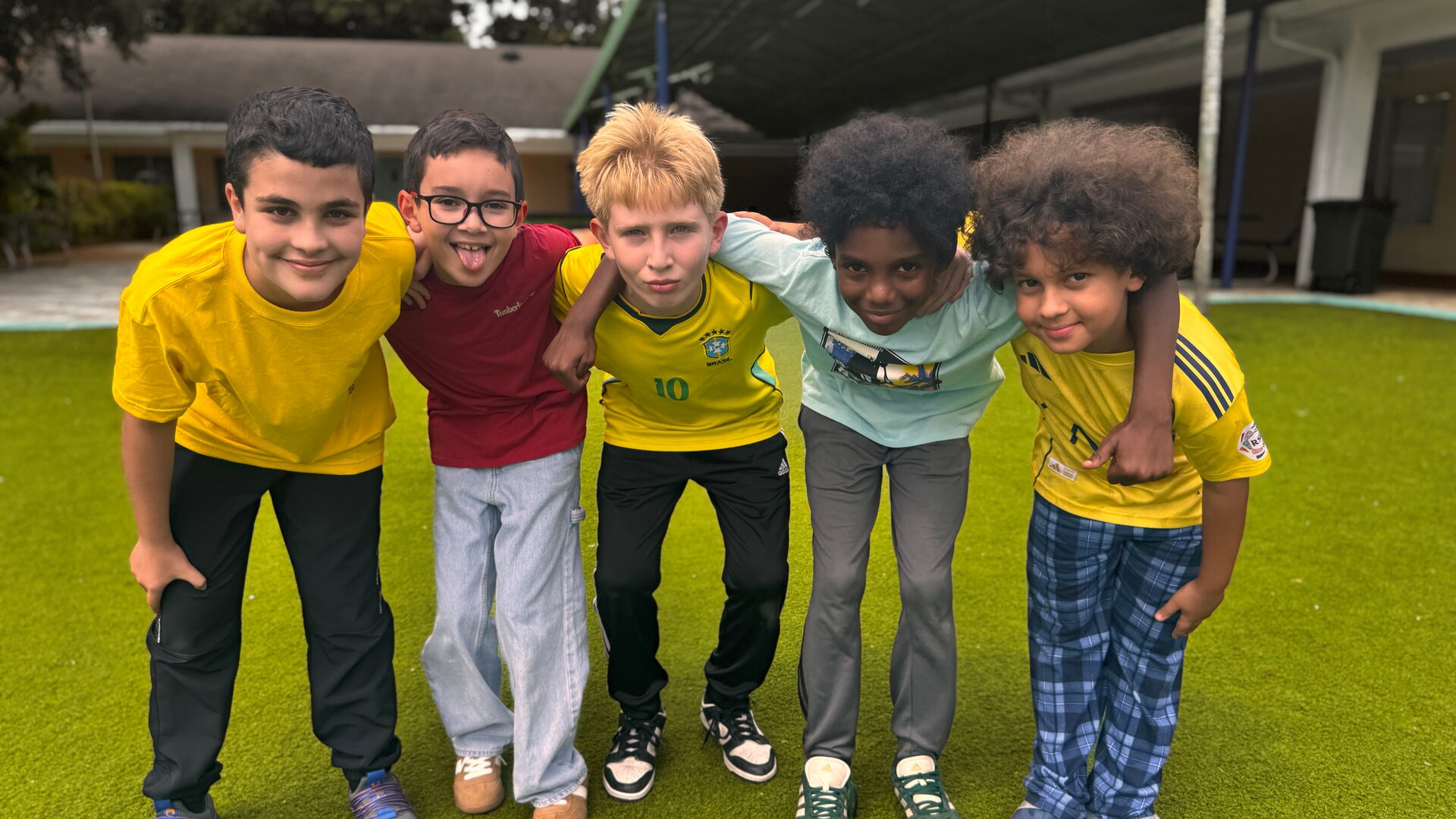 Five young students in jerseys and T-shirts link arms and smile on the turf.
