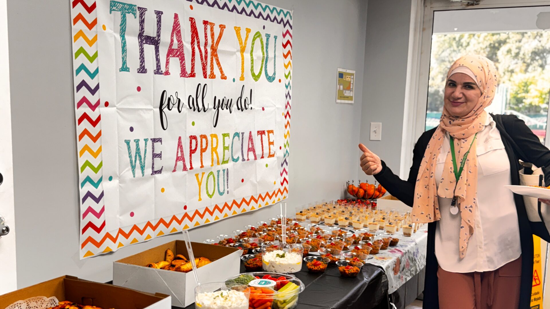 A staff member gives a thumbs-up beside the breakfast spread and the thank-you banner.