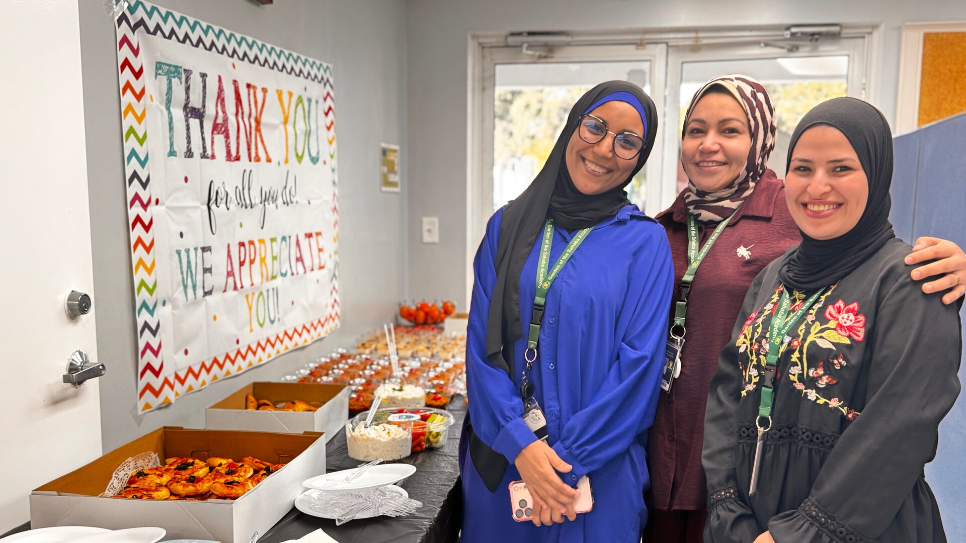Three staff members smile together beside the breakfast table and the thank-you banner.