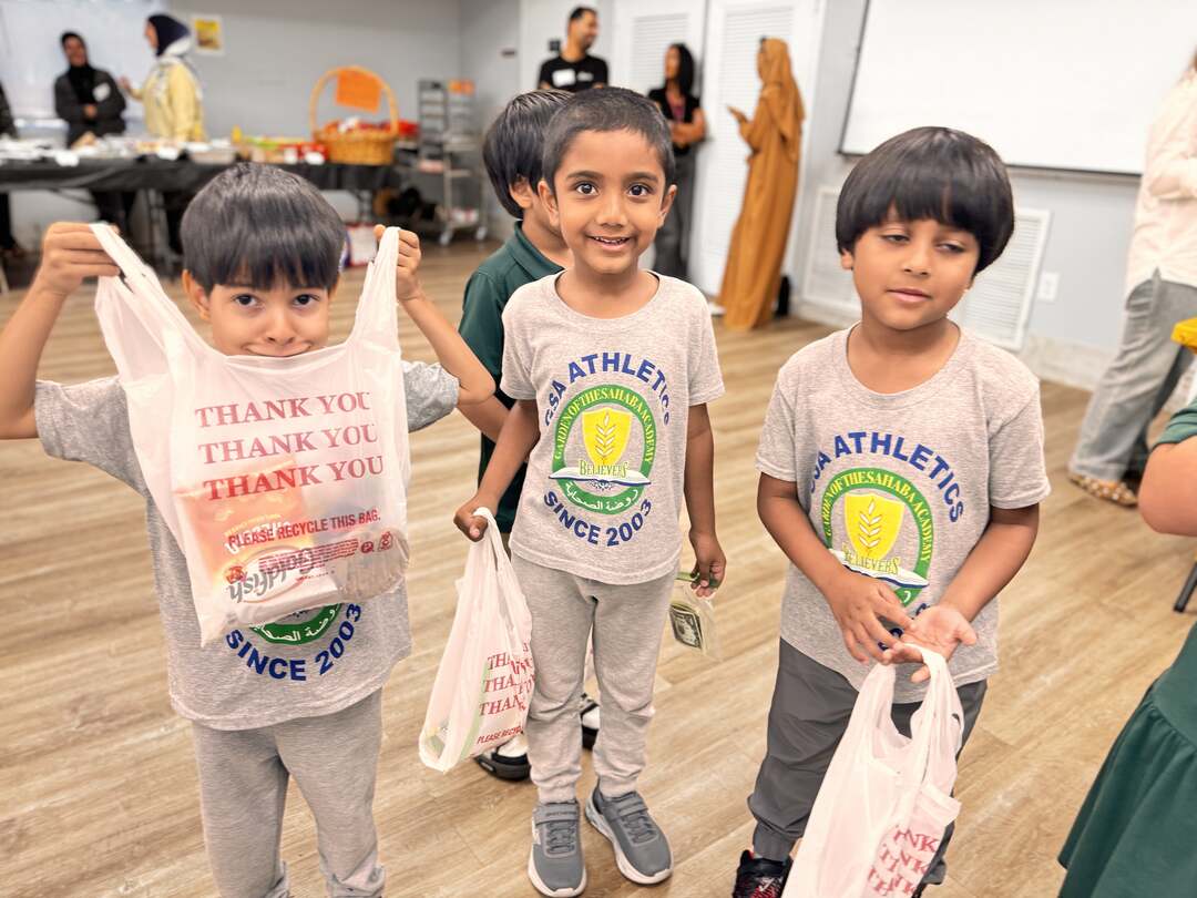 Three young students hold up their bags of goodies, one peeking over a Thank You bag