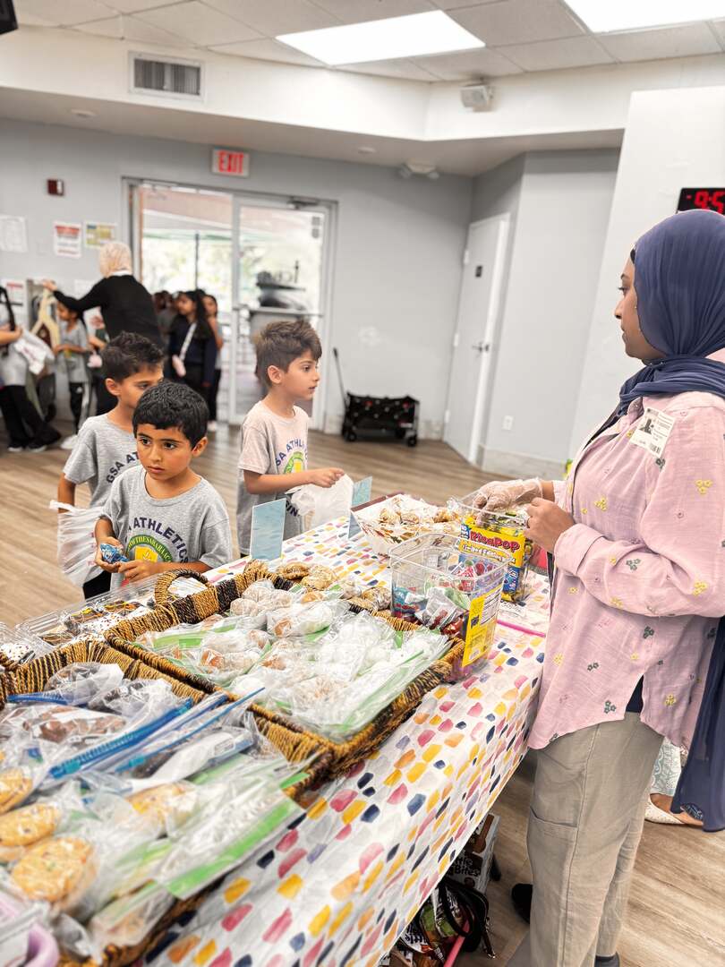 A volunteer in a pink top looks after young shoppers at the cookie table