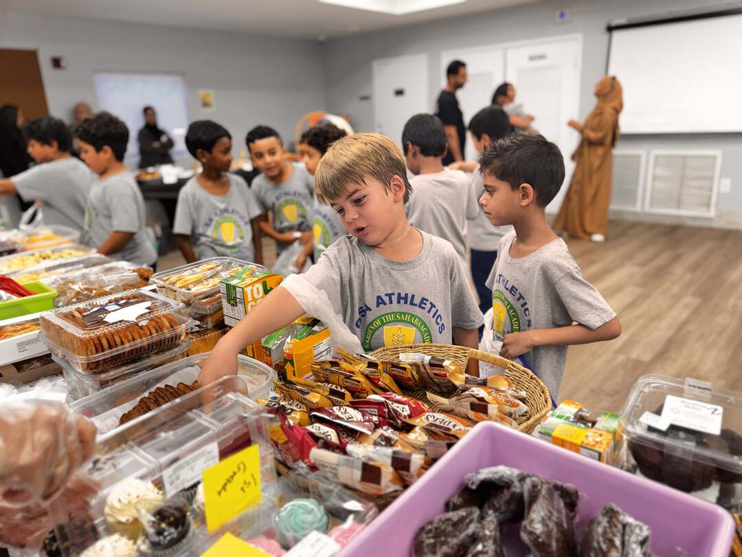 A young student reaches into a basket of snacks as classmates line up