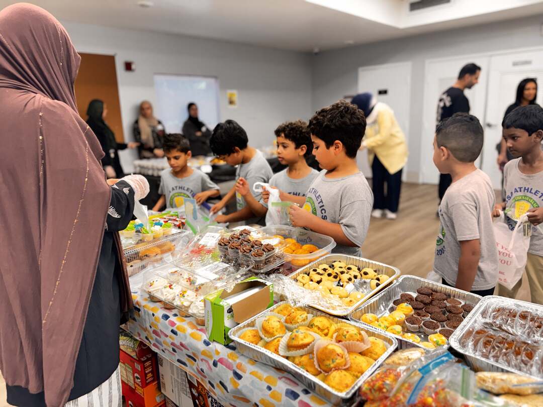 Classmates fill their bags beside trays of muffins and brownies