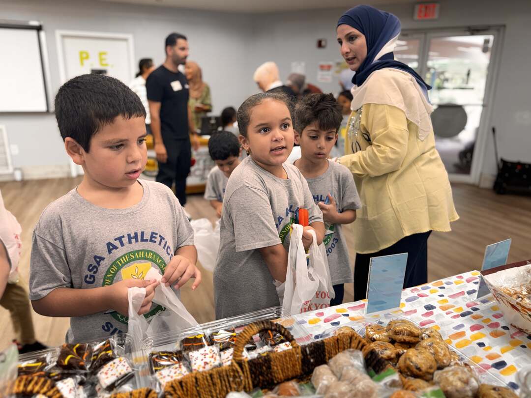 Three young shoppers hold open their bags at the cookie table