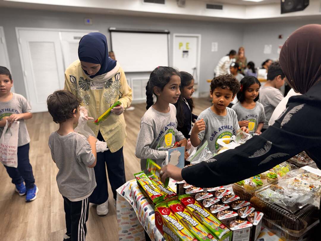 Young students choose packaged treats while volunteers help out