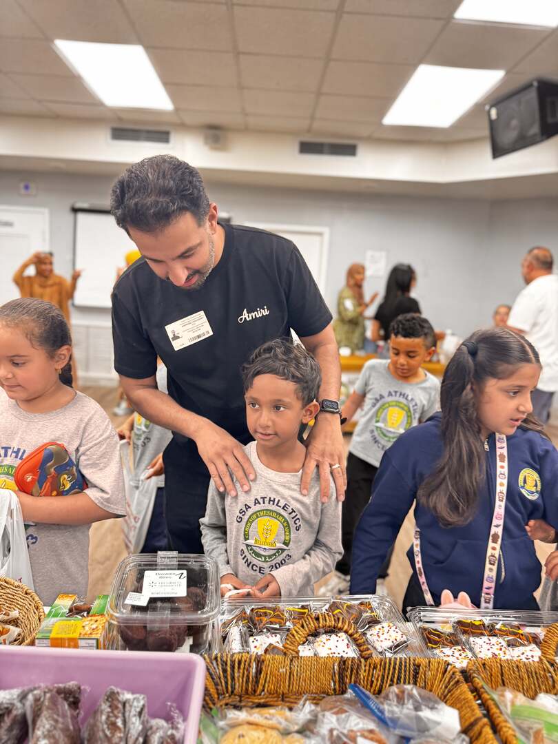 A volunteer rests a hand on a young student's shoulders at the treat table