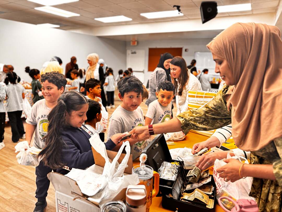 A volunteer collects payment at the cash table as a line of smiling students waits its turn
