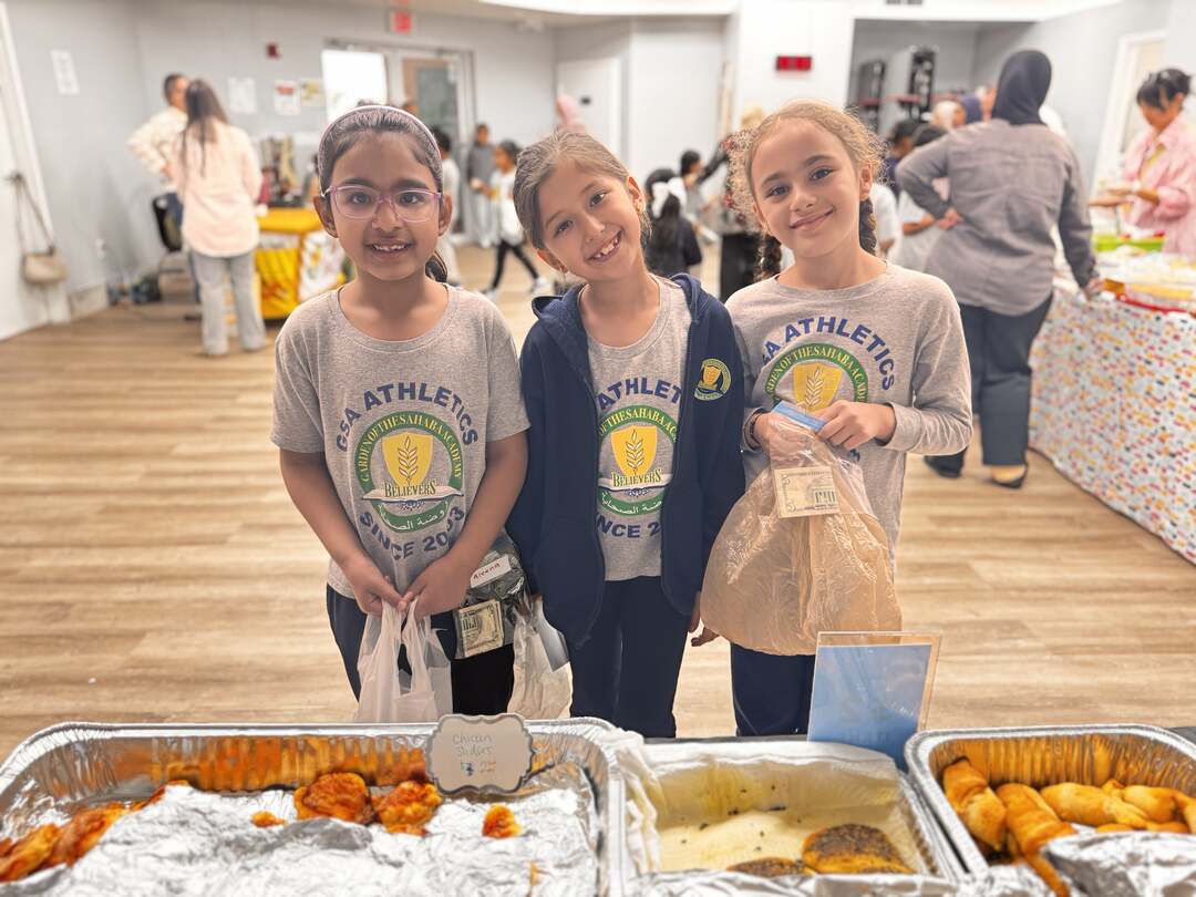 Three smiling students line up at a table of savory pastries