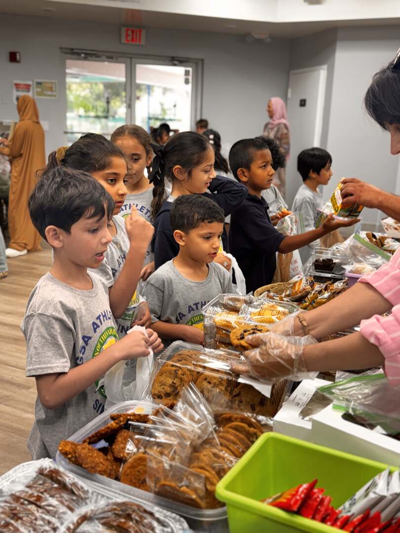 A line of young students waits as gloved hands pass out cookies