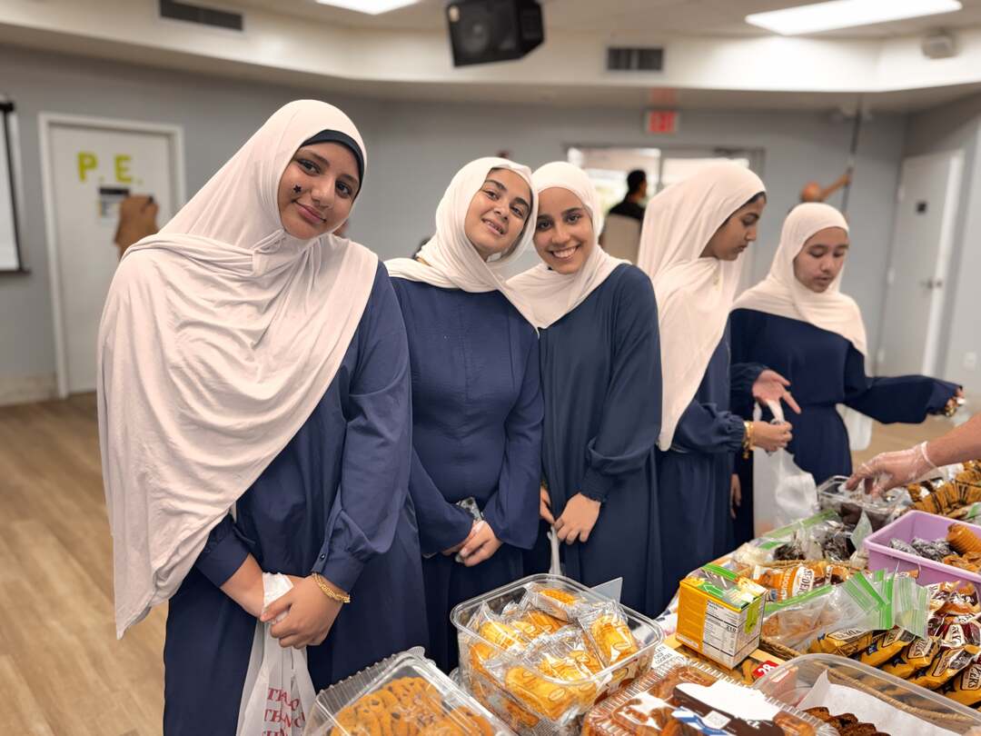 A row of older students smiles beside a table of snacks and baked goods