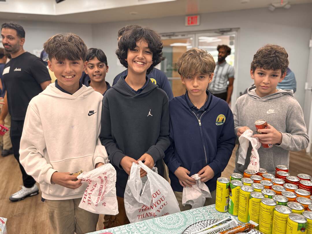 A group of students grins at the drinks table, bags of goodies in hand