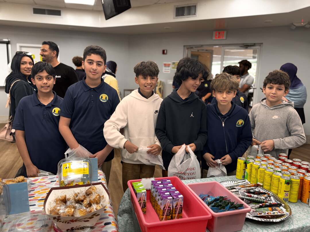 A row of older students stands behind the drinks and snack table