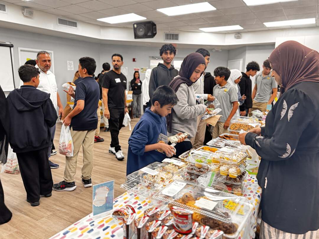 Students browse a long table of cupcakes, cookies and sweets as the room fills with shoppers