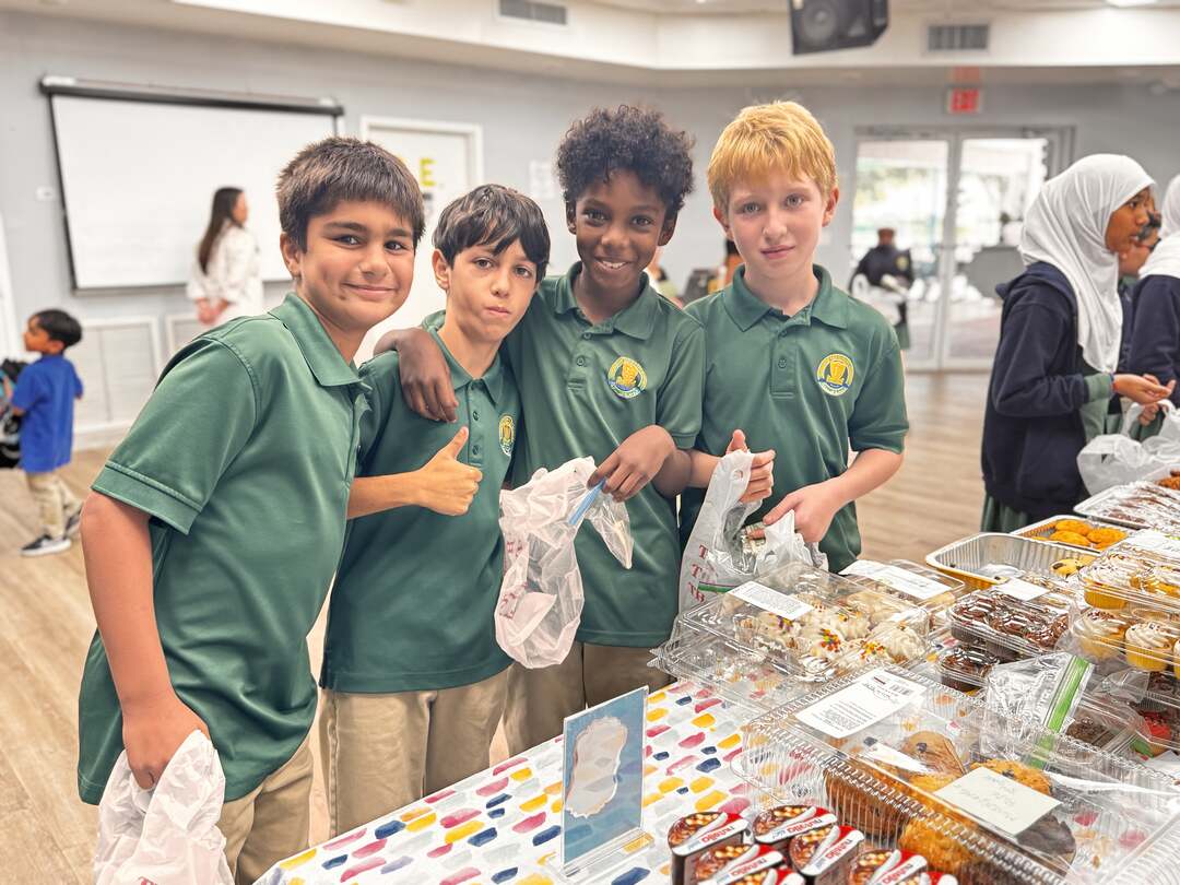 Four students in green polos give a thumbs-up at the dessert table